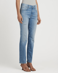 A person stands against a white background wearing Edwin's Bree in Reverie light blue slim straight leg, ankle-length jeans with subtle fading and a small distressed detail near the pocket, paired with brown heeled sandals.