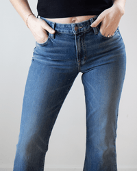 A person in Edwin’s Lark Ankle in Geary jeans and a black top stands with hands in their pockets, showing a casual style.