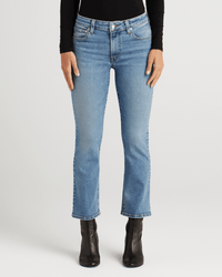 A person wearing Edwin’s Lark Ankle in Lombard—ankle-length, light blue mid-rise cropped boot cut jeans—with a black long-sleeve top and black ankle boots stands against a plain white background.