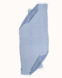 The Épice Solid Scarf in Forget Me Not, a light blue linen piece with fringed edges and crisp white trim, is shown laid flat with two corners folded to reveal the reverse side.