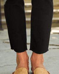 Close-up of a person wearing Frank & Eileen's Derry Illusion Pull On Pants in Black Denim and tan loafers, standing on a stone surface with blurred steps in the background.