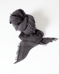 The Grisal Love Cashmere Scarf in Brown Top X Charcoal, featuring frayed edges, is loosely knotted and displayed on a white surface.