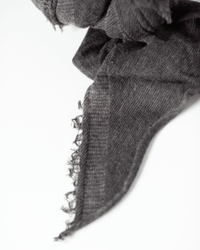 A close-up of the Grisal Love Cashmere Scarf in Brown Top X Charcoal against a white background highlights its frayed edges and heirloom-quality craftsmanship.
