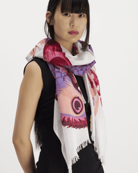 A woman with long dark hair and bangs wears a black sleeveless dress and the Scarf 100 Toucan in Pink by Inoui Editions, featuring vibrant patterns, draped around her neck against a plain white background.