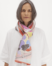 A woman with long gray hair wears a white shirt and the Inoui Editions Scarf 100 Yoga in Multicolor. She stands against a plain white background, looking directly at the camera with a neutral expression.