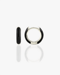 The Kris Nations Enamel Huggie Hoops in Black & Sterling Silver are shown—one earring upright and the other flat—highlighting their sleek, shiny enamel finish on a reflective white surface.