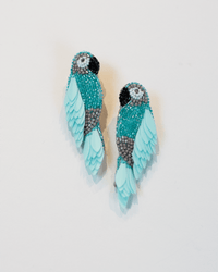 A pair of Olivia Dar Ara Earrings in Mint, shaped like parrots with detailed beadwork in blue, gray, white, and black, displayed on a plain white background.