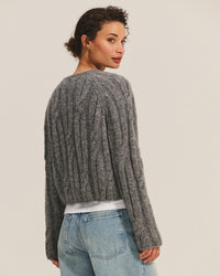 A person with short curly hair wears the Velvet by Graham & Spencer Marina Long Sleeve Crew Top in Heather Grey and light blue jeans, standing with their back slightly turned and looking over their shoulder against a plain background.