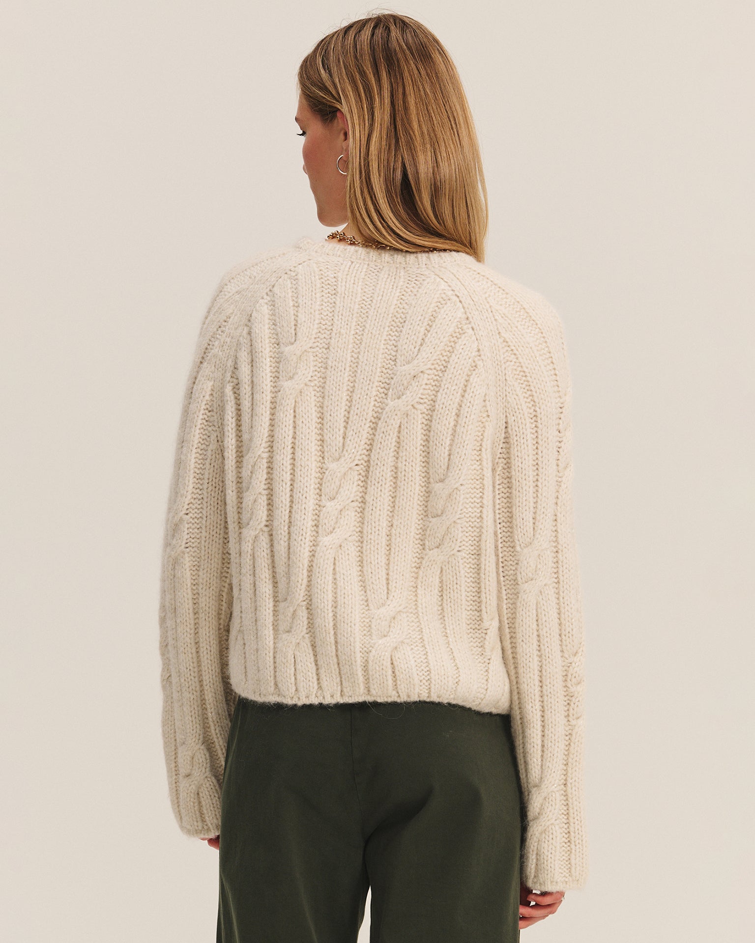 A person with shoulder-length light brown hair is shown from the back, wearing the Marina Long Sleeve Crew Top in Ivory by Velvet by Graham & Spencer and olive green pants against a plain light background.