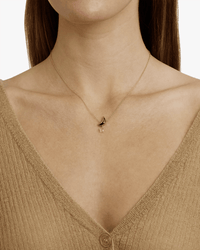 A woman wears a tan, ribbed V-neck top with the Chan Luu Moon & Star Necklace in Black Mix. Her face is out of frame, highlighting the sparkling charm and delicate 18k gold plated sterling silver details.
