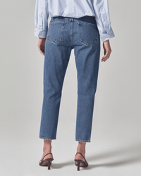 A person stands facing away, wearing a blue and white striped shirt, Citizens of Humanity Charlotte High Rise Straight in First Class jeans, and brown heeled sandals against a plain light background.