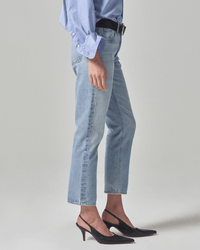 A person wearing a light blue button-up shirt, Citizens of Humanity Isla Low Rise Straight in Spector jeans, and black slingback heels stands against a plain light gray background.