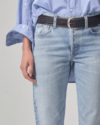 A person wearing a light blue button-up shirt and Citizens of Humanity Isla Low Rise Straight in Spector jeans. Only the torso and upper legs are visible; jeans feature a vintage fit, paired with a black woven belt with a silver buckle.