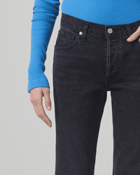 A person wears a bright blue, long-sleeved ribbed top with Citizens of Humanity's Neve Low Slung Relaxed in Voila pants. Only the torso and upper legs are visible against a light gray background.