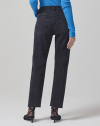 A person shown from the back wears Citizens of Humanity's Neve Low Slung Relaxed in Voila jeans with a bright blue ribbed long-sleeve top and black heeled sandals, standing with one arm relaxed.