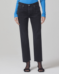 A person stands against a plain light background wearing a bright blue ribbed long-sleeve top, Citizens of Humanity’s Neve Low Slung Relaxed in Voila pants, and black open-toe sandals with sheer black socks.