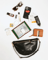 Flat lay of the Clare V. Grande Fanny in Black Nouveau with sunglasses, medicine, phone, wallet, AirPods, lotion, lipstick, pen, metro cards, receipts & gum arranged around it. Includes an adjustable strap for comfort.