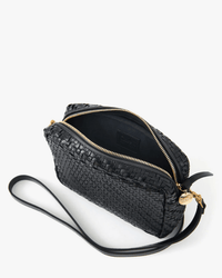 The Clare V. Midi Sac in Black Woven Zig-Zag is a crossbody bag with a gold zipper and long strap, shown from above partially open on a white background.