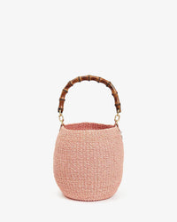 The Clare V. Pot de Miel w/ Bamboo Handle in Blush is a small, round, handwoven straw basket purse with a curved bamboo top handle, shown against a plain white background.