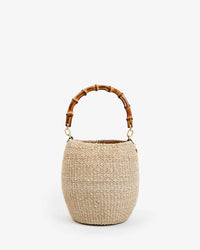 The Pot de Miel w/ Bamboo Top Handle in Cream by Clare V. is a round handwoven straw bag with a curved bamboo top handle, shown against a plain white background.