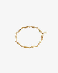 The Clare V. Sardine Link Bracelet in Vintage Gold features linked fish-shaped charms and a small oval tag, offering timeless style on a plain white background.