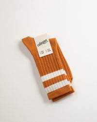 The Nico Varsity Socks in Terracotta by Collegien feature orange ribbing with two white stripes near the top and come labeled "made in France"—ideal for achieving a sporty sock look.