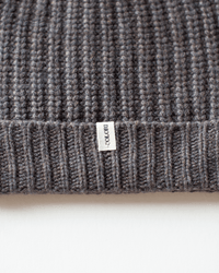 Close-up of a ribbed, dark gray knit fabric from the Ribbed Beanie in Beaver by COLORI, featuring a small white tag sewn into the seam.