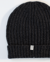 A close-up of the COLORI Ribbed Beanie in Carbon, featuring a folded brim and a small white tag on the edge, shown against a white background.
