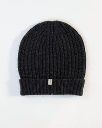 The COLORI Ribbed Beanie in Carbon features a dark gray ribbed knit with a folded cuff and a small rectangular tag, shown flat on a white background.