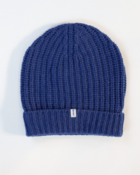 The COLORI Ribbed Beanie in Neptune is a blue winter hat with a folded brim and a small white tag on the front, shown on a white background.