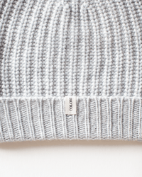 Close-up of the COLORI Ribbed Beanie in Shark, featuring a gray ribbed knit and a small vertical "COLORI" tag sewn into the bottom hem. Set against a plain off-white background.