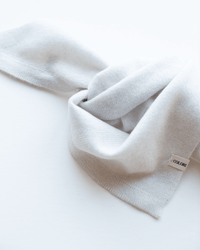 A lightweight COLORI Small Triangle Bandana in Stucco, loosely folded on a white surface with its tag visible, offers an elegant and comfortable accessory for any outfit.