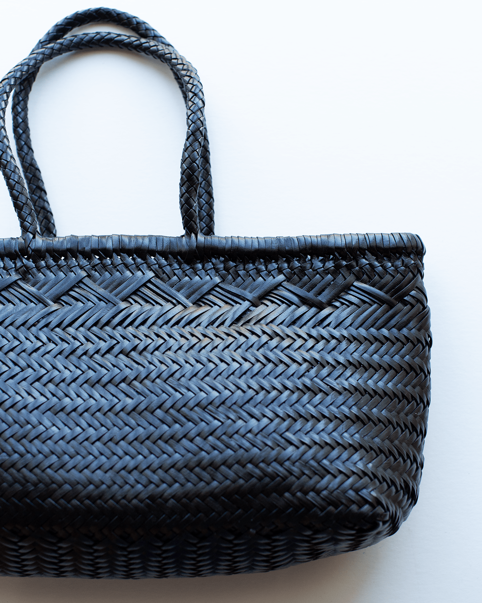 A close-up of the Dragon Diffusion Bamboo Triple Jump - Large - 6 Lines in Black, showcasing its handwoven buffalo leather, twin handles, and intricate herringbone pattern against a white background. Only part of the artisan bag is shown.