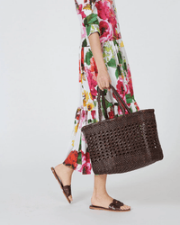 A person in a white floral dress and brown sandals holds the Dragon Diffusion Cannage Max tote in Dark Brown. The cropped image shows only the lower half of the body against a plain background.