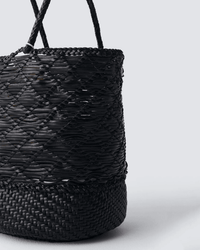 Close-up of the Dragon Diffusion Corso Bucket Bag in Black, showcasing braided handles, a solid base, and intricate weaving patterns against a plain gray background.