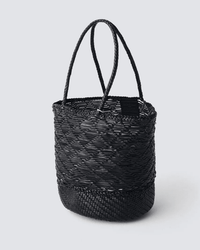 The Corso Bucket Bag in Black by Dragon Diffusion is a cylindrical woven basket bag with two braided handles and a textured pattern, shown on a light gray background.