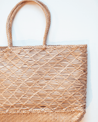 A close-up of the Dragon Diffusion EW Corso Bag in Natural, featuring two handles, a unique woven crosshatch design, and a textured bottom edge, set against a light background.