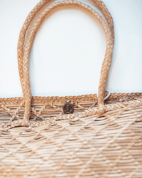 Close-up of the Dragon Diffusion EW Corso Bag in Natural with braided handles against a light background. This handmade bag features a woven crosshatch design, textured pattern, and a small round clasp at the top center.