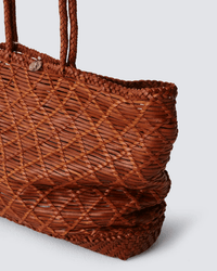 A close-up of the Dragon Diffusion EW Corso Bag in Tan, featuring brown woven leather with crisscrossed patterns and two braided handles, set against a light gray background, showcasing timeless style and craftsmanship.