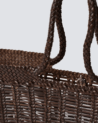 Close-up of the Dragon Diffusion Window Basket in Dark Brown, featuring hand-woven texture, braided handles, and a round metallic charm on the front that highlights its intricate weave.