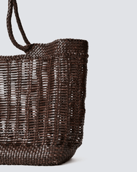 A close-up of the Dragon Diffusion Window Basket in Dark Brown, featuring two handles and a detailed hand-woven pattern, is shown against a plain light gray background with a partial side view visible.