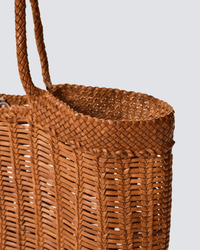 Close-up of the Window Basket in Tan by Dragon Diffusion—a hand-woven basket bag with braided handles and intricate pattern, displayed against a plain light grey background, highlighting its artisanal craftsmanship.