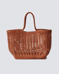 The Window Basket in Tan by Dragon Diffusion, a hand-woven bag with two sturdy handles and an open, airy weave over a flat rectangular base, is displayed against a plain light gray background.