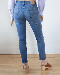 Person standing on a light wooden floor, shown from behind, wearing Edwin’s Bree in Enigmatic jeans, a light blue and white striped shirt, and brown heeled clogs.