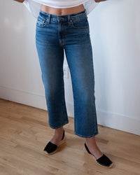 A person wearing Edwin's Marli Wide Leg Ankle in Bengal jeans, a white top, and black espadrille sandals stands on a wooden floor by a white wall. Their head and upper body are out of frame.