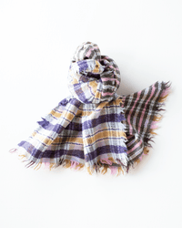 The Épice Check Blanket Scarf in Pink, crafted from 100% wool with frayed edges, showcases pink, purple, yellow, and black stripes and is styled in a loose knot on a white background.