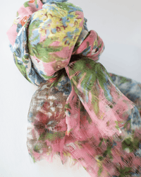 A close-up of the Fleur 1 Scarf in Peony by Épice, loosely tied and showcasing a translucent hand screen printed pattern with pink, green, blue, and yellow hues on 100% wool.