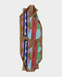 The Épice Linen/Cttn Lrg Squiggle Scarf in Pecan is a handwoven rectangular scarf with brown edges and abstract blue, purple, red, green, and cream shapes on a light brown background. Made from linen and cotton with neatly folded corners.