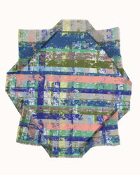 The Painterly Plaid Bandana in Green by Épice features layered, irregular stripes in blue, green, yellow, pink, and brown, folded into a geometric star shape on a plain white background.