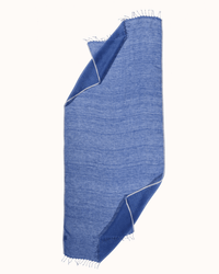 The Épice Solid Scarf in Cornflower is a light blue linen scarf with white piping and frayed edges, shown laid flat with two corners folded inward on a white background.